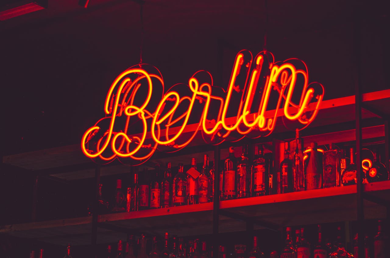 Illuminated Berlin neon sign above a shelf of alcohol bottles in a bar setting.